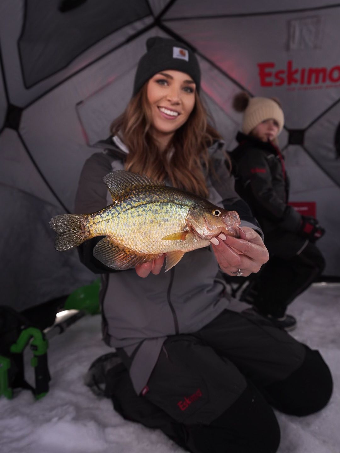 Ice fishing scene inside a shelter with someone displaying their freshly caught fish.