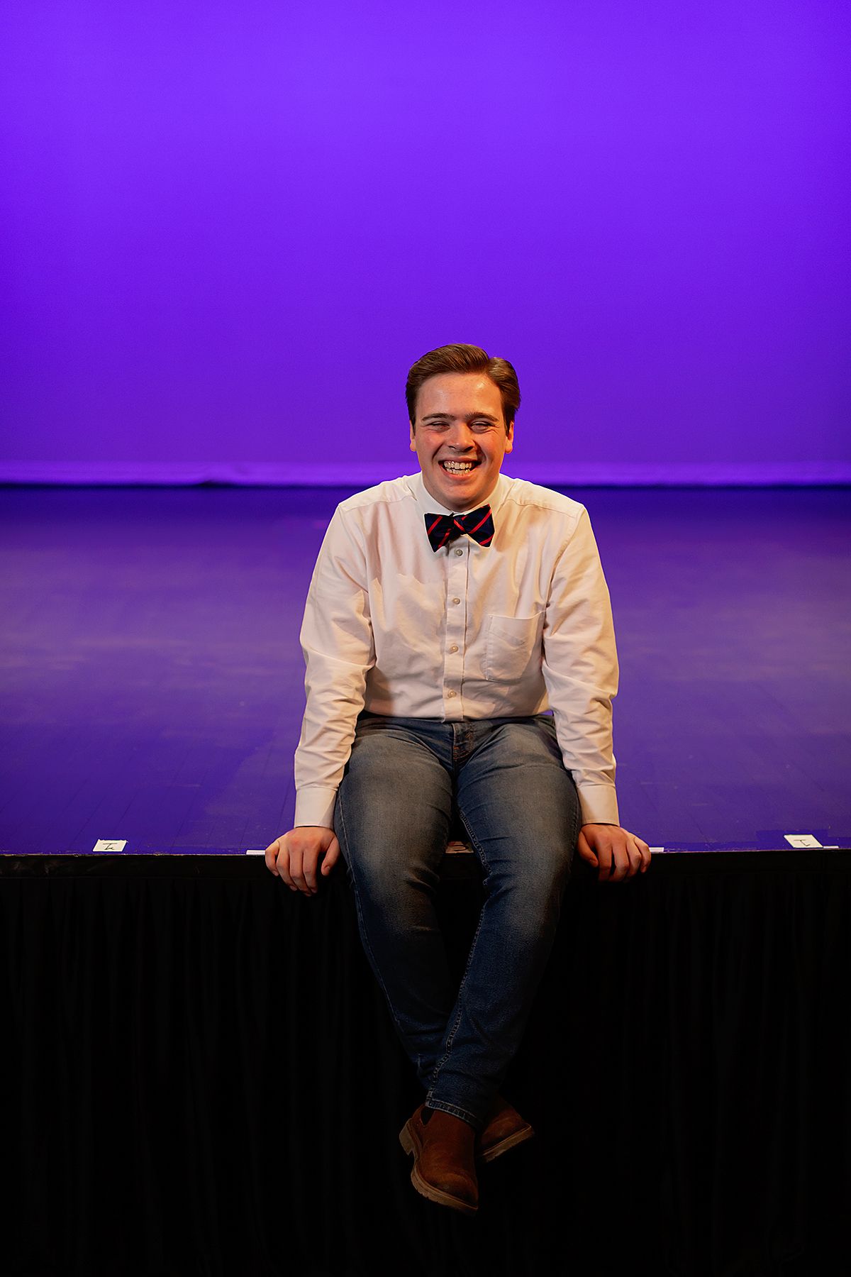 Male teen wearing a button up and bow tie on the stage of the Ned McWherter Theater in Jackson, TN. Senior picture by MegMc Photography