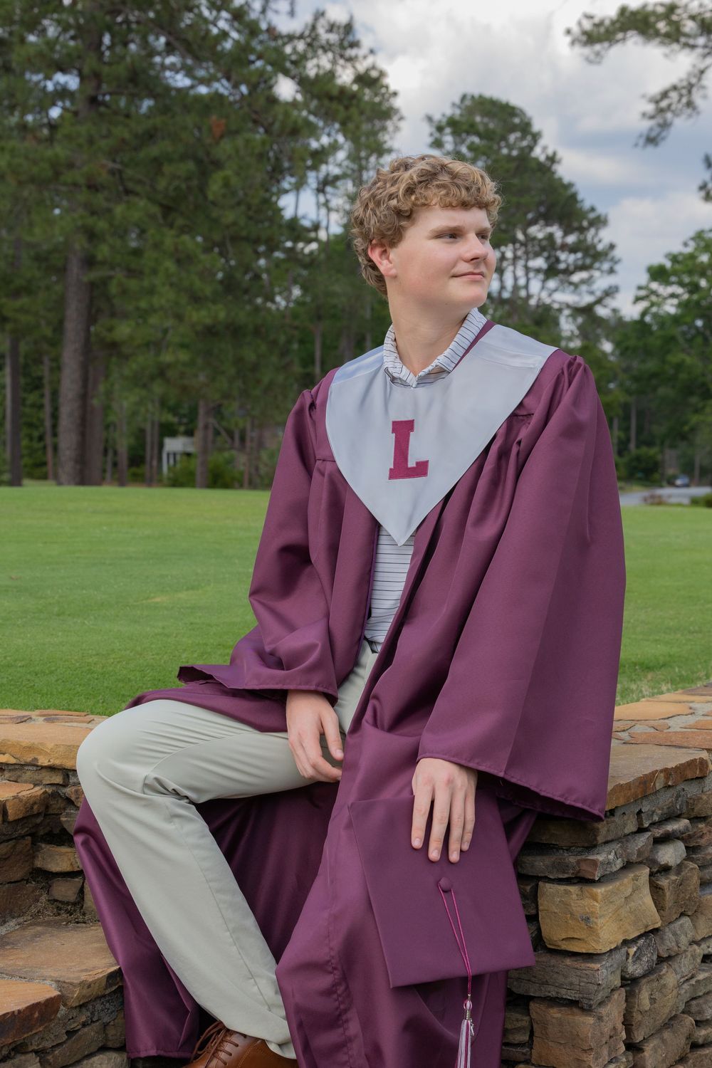 Portrait photos across outdoor stone wall showing graduate posing in maroon gown and grey shirt against green landscape.