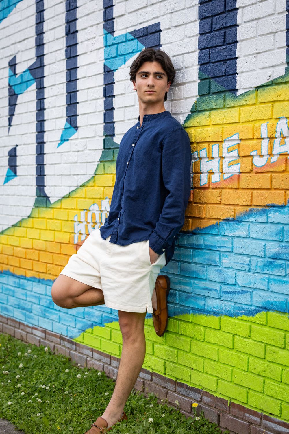 A person in navy shirt and white shorts poses against a colorful street art mural.