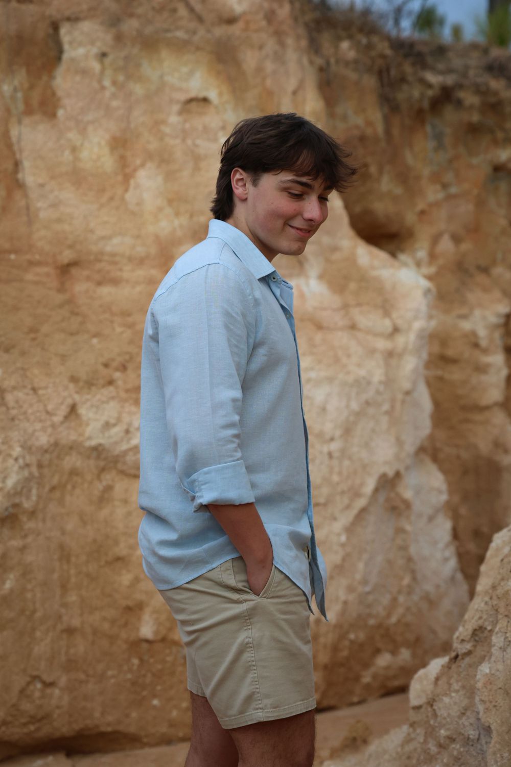 Person in light blue button-down shirt poses against tan rock formation outdoors.