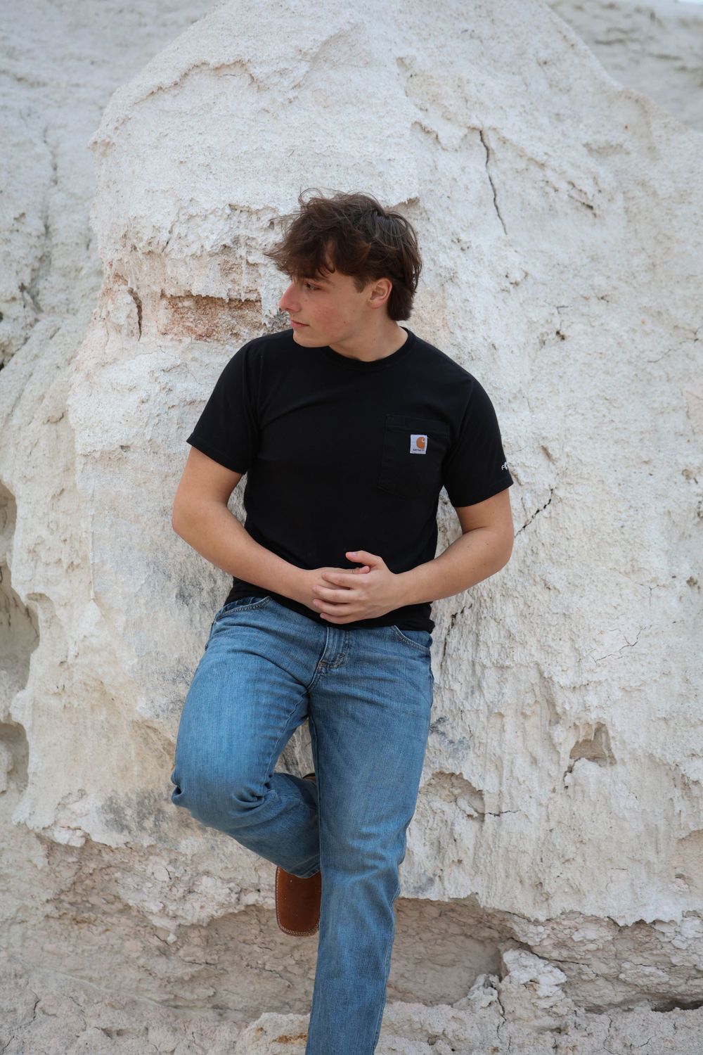Person in black t-shirt and jeans leans against white limestone rock wall.