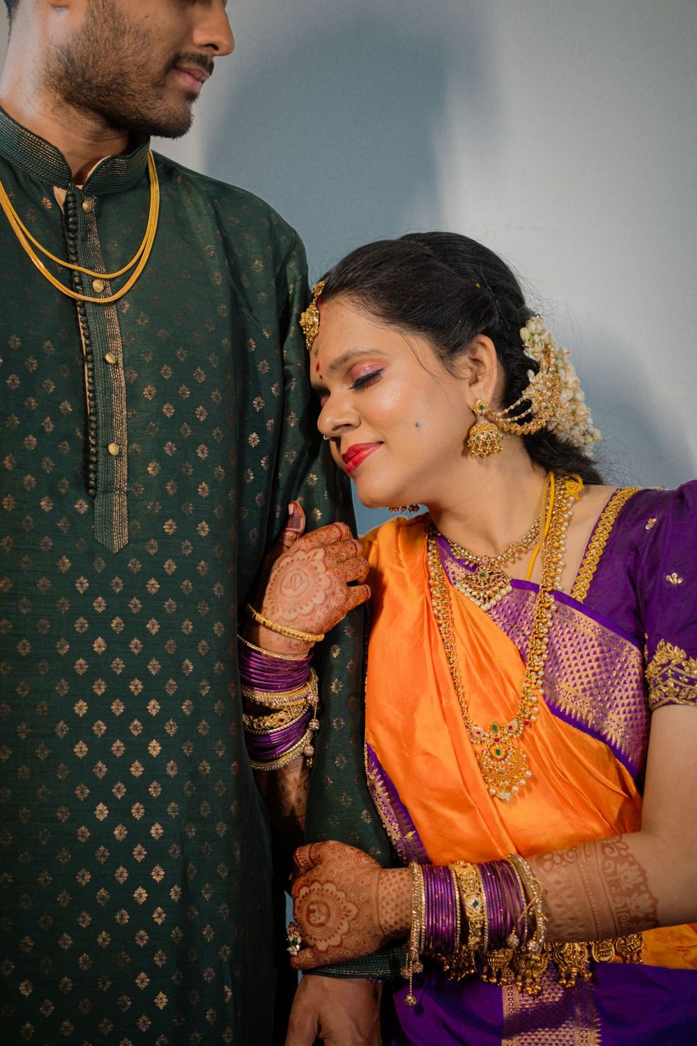 Couple in traditional Indian wedding attire with bride wearing orange and purple saree, and groom in dark green kurta.