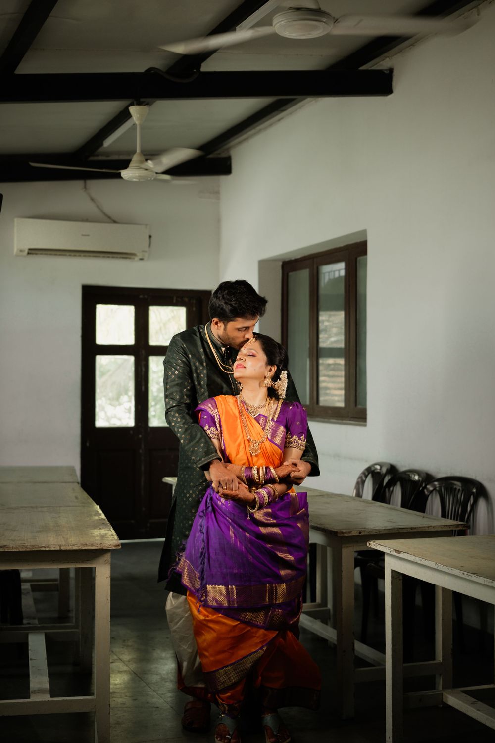 A romantic scene in a room with exposed beams showing a couple in traditional Indian clothing embracing.