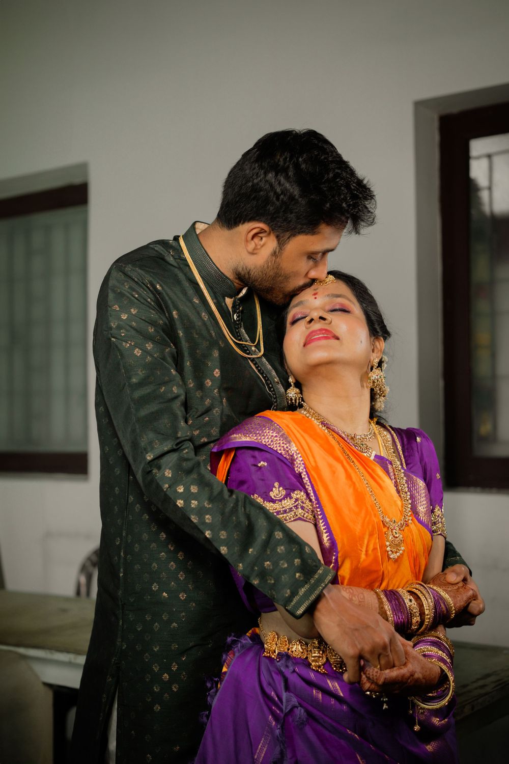 A couple in traditional Indian attire share an intimate moment with the woman wearing a bright orange and purple saree.