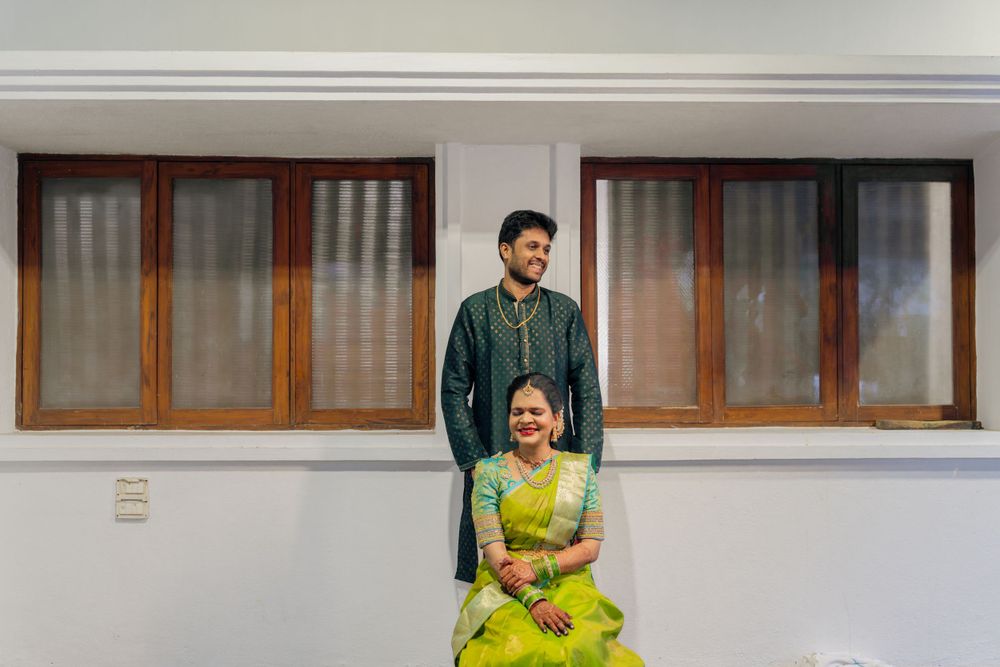 A couple poses in front of a building with large windows, the person seated wearing a vibrant yellow dress.