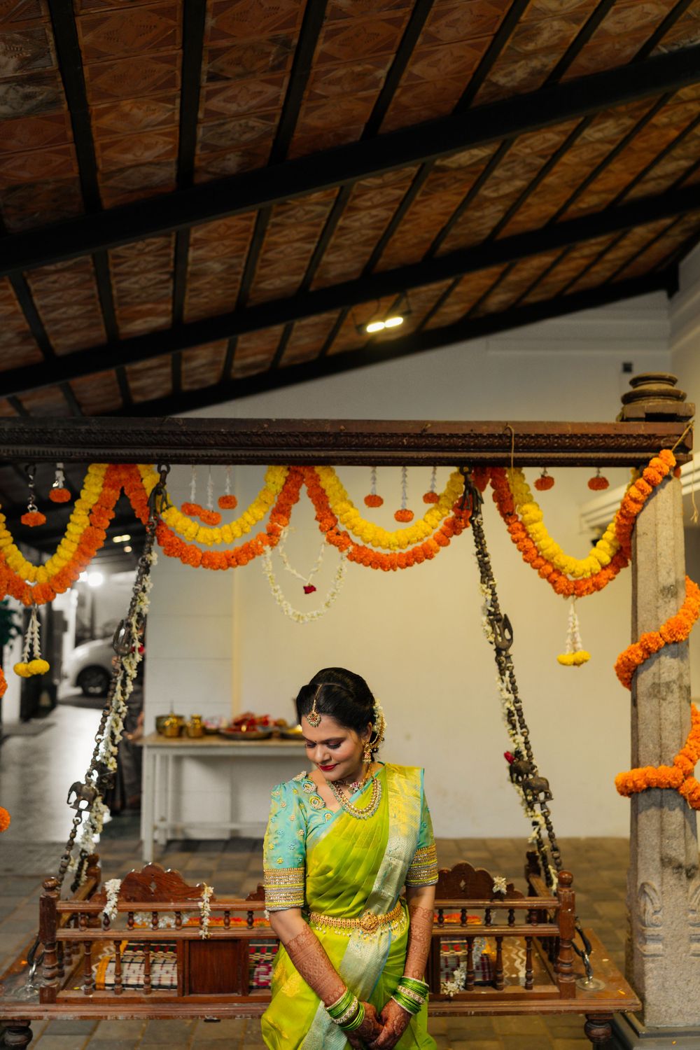 Traditional decor with orange and yellow marigold garlands hanging from wooden beamed ceiling in Indian celebration setting.