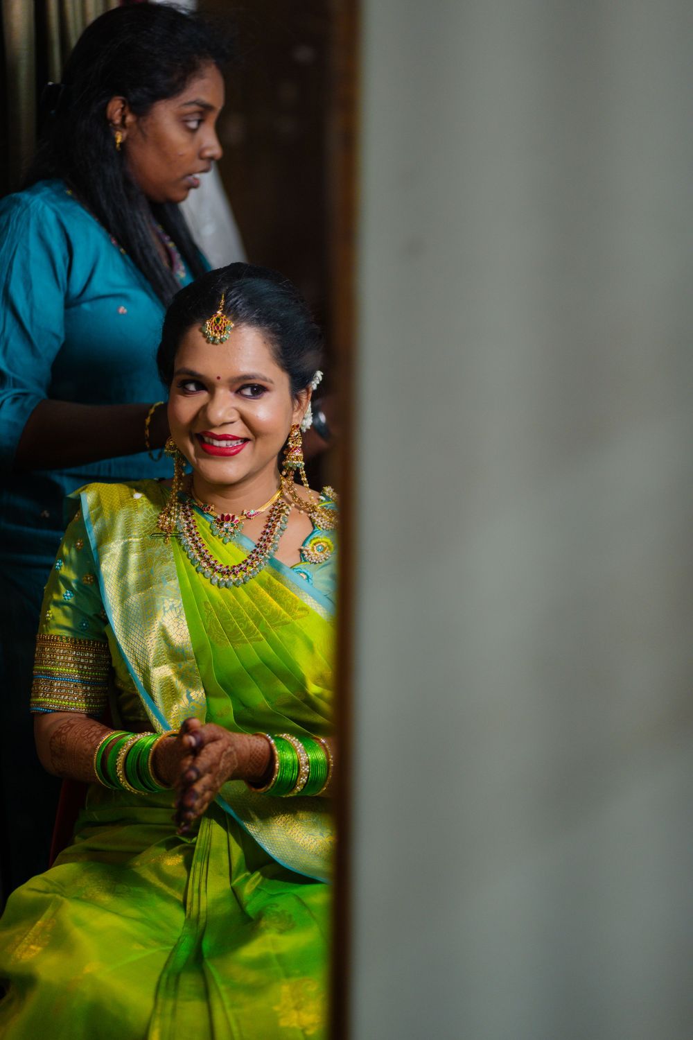 Traditional South Indian bride in a lime green silk saree with gold jewelry getting ready.