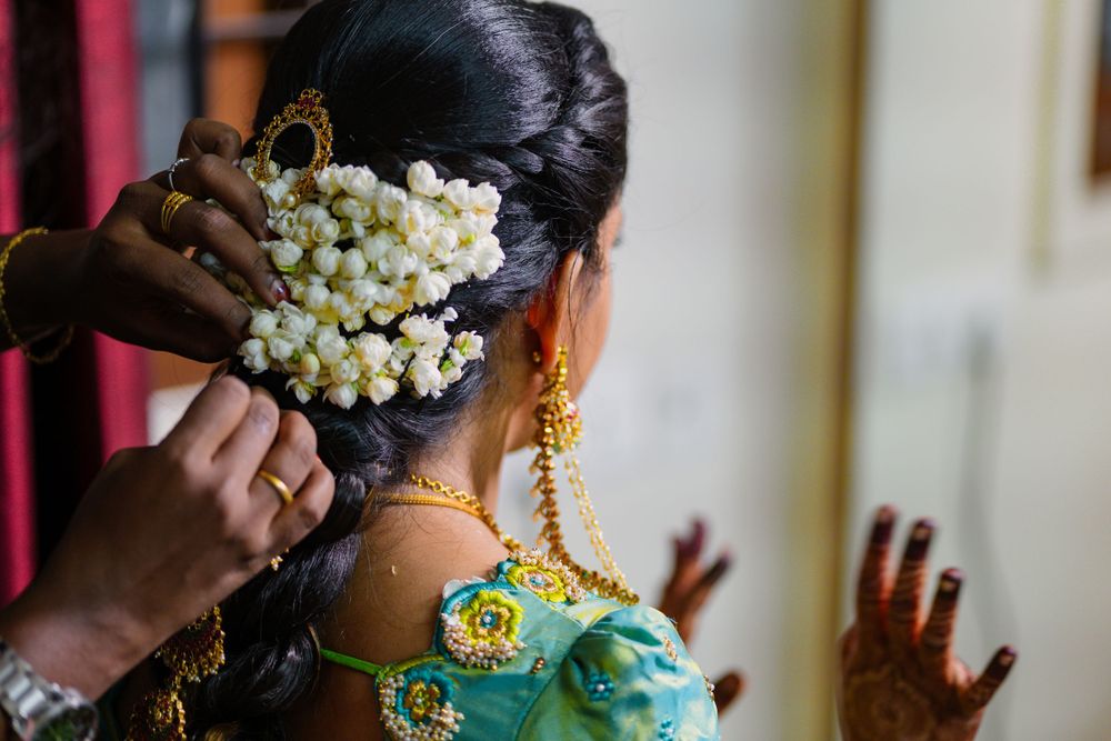 Traditional white jasmine flowers being pinned into dark hair with gold temple jewelry and green silk saree.