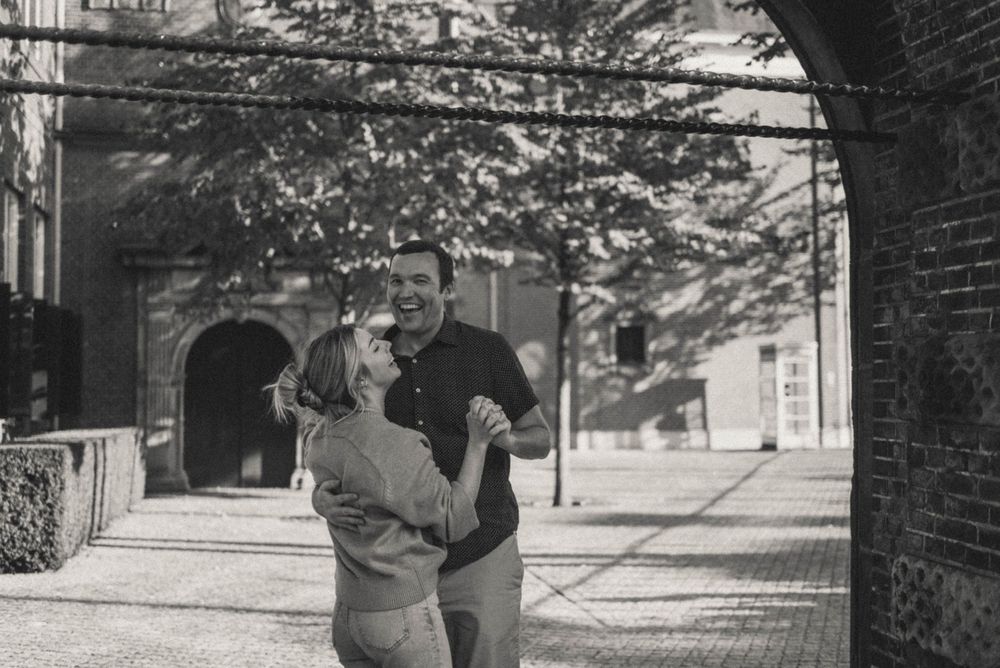 A couple strolls beneath a vintage brick archway in a black and white photograph.