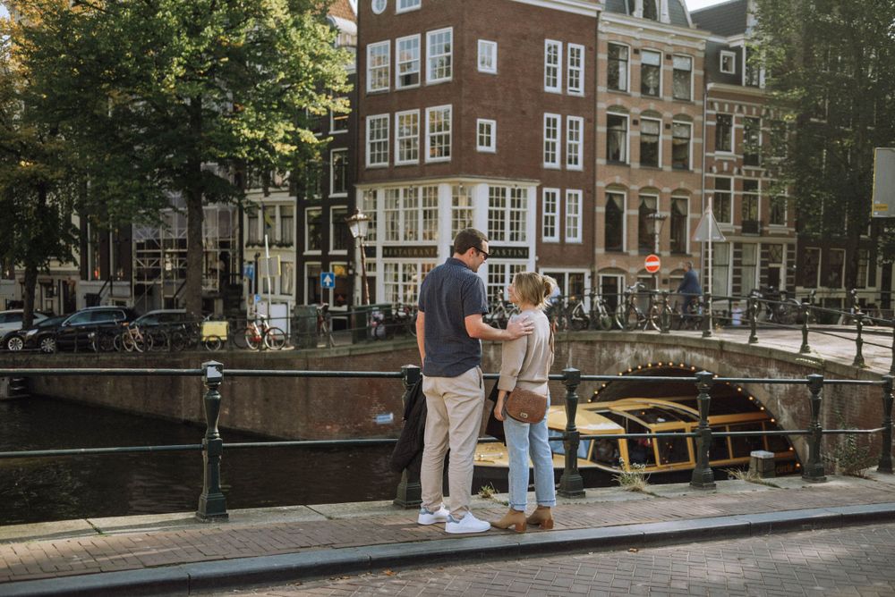 Couple walking along Amsterdam canal with traditional architecture in background.