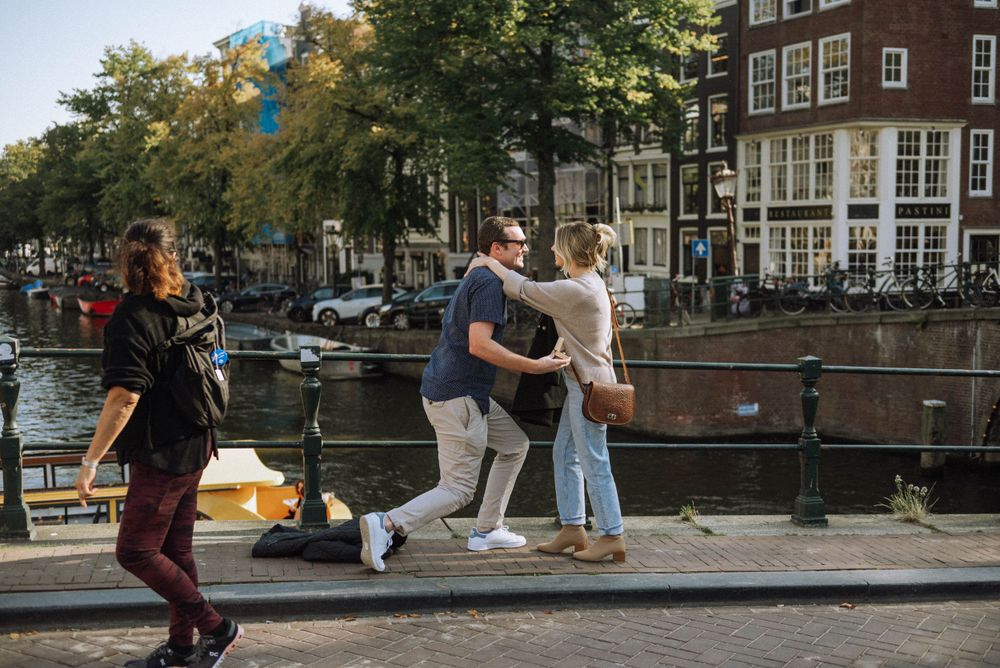 Urban scene along Amsterdam canal with pedestrians and historic buildings.