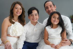A studio portrait of a family of four wearing coordinated white outfits against a grey background.