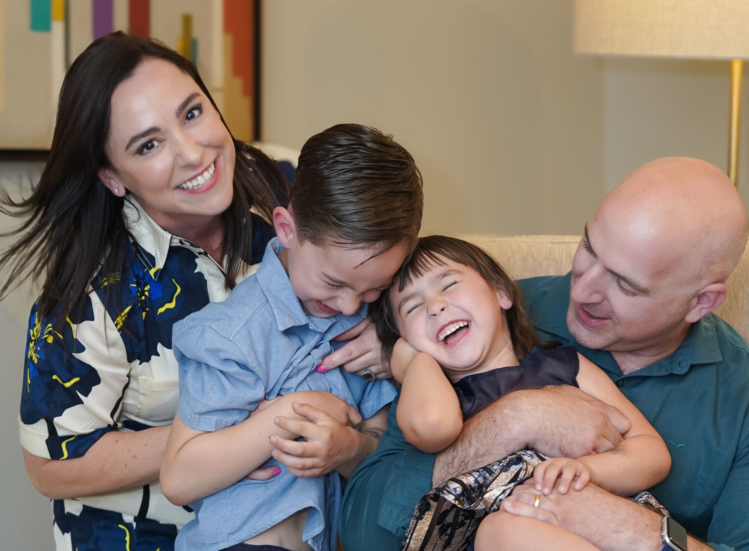Family sharing playful moment on couch while tickling and laughing together.