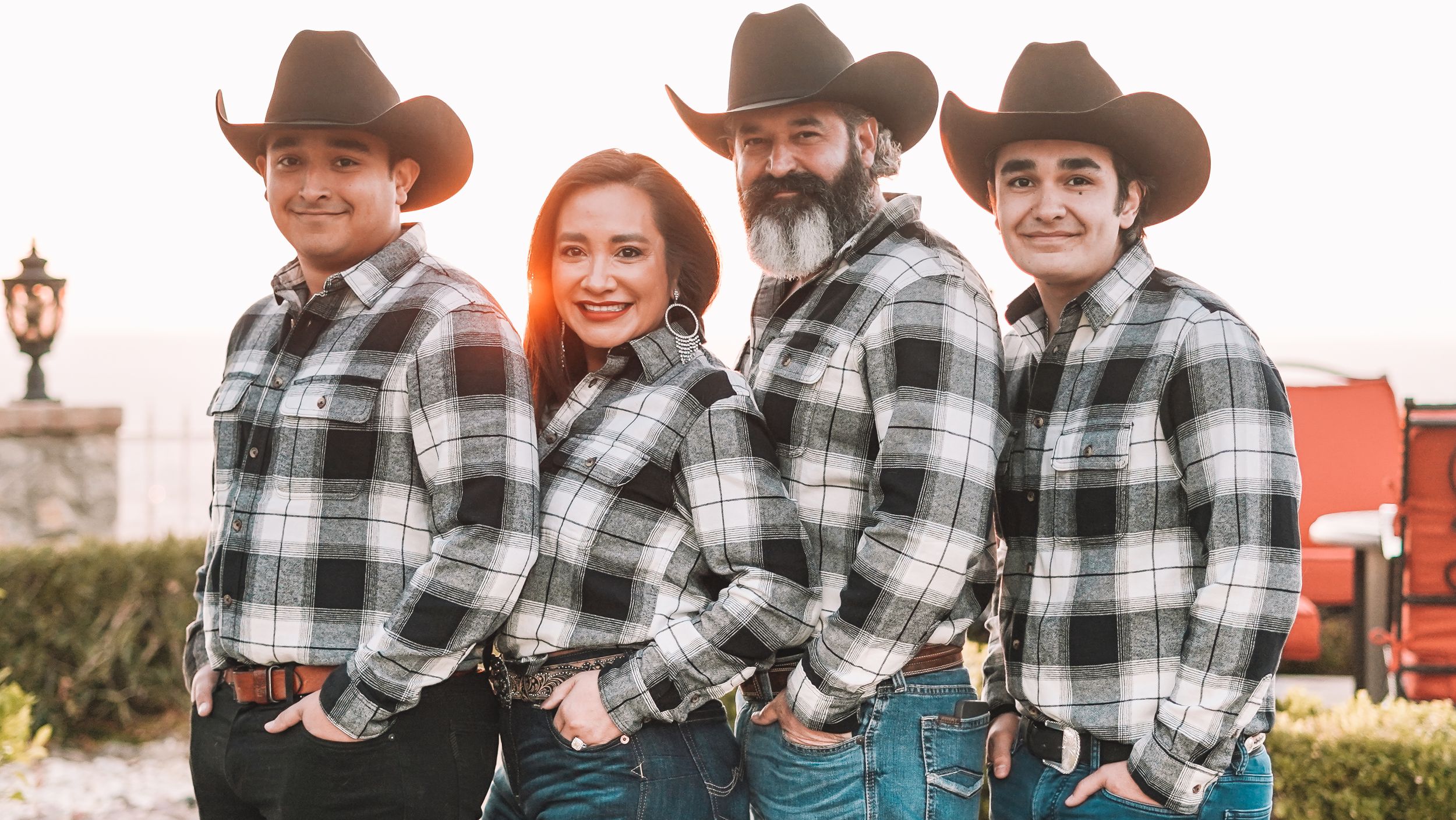 Family in matching plaid shirts and cowboy hats pose together outdoors.