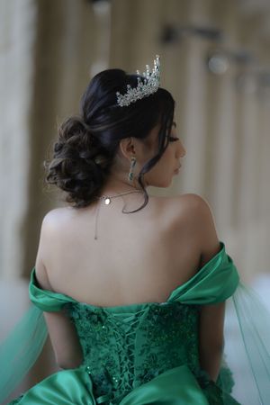 Back view of an elegant emerald green ball gown with corset detail and crystal tiara.