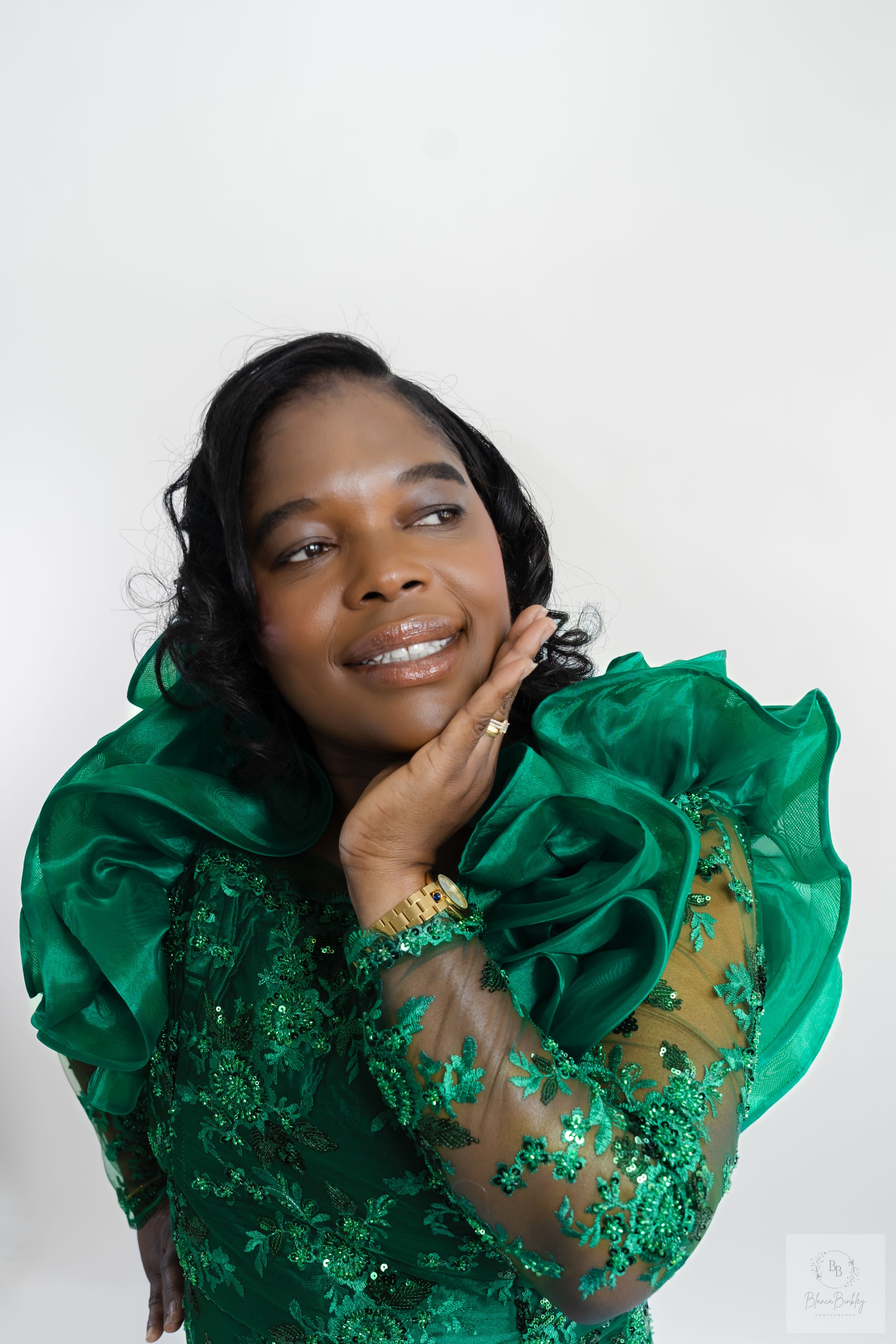 Woman in elegant emerald green dress poses against white background with joyful smile.
