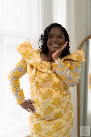 A person wearing a vibrant yellow floral dress poses cheerfully against a bright indoor setting.