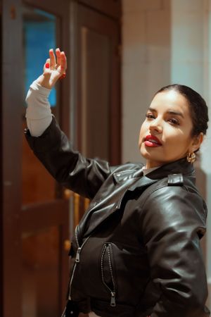 A stylish person in black leather jacket strikes a confident pose with raised arm.