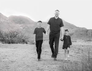 A black and white photograph of three people walking together in a desert landscape.