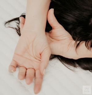Artistic closeup of an outstretched hand against white bedding.