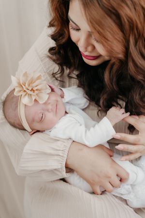 A mother lovingly gazes at her sleeping newborn baby wearing a floral headband.