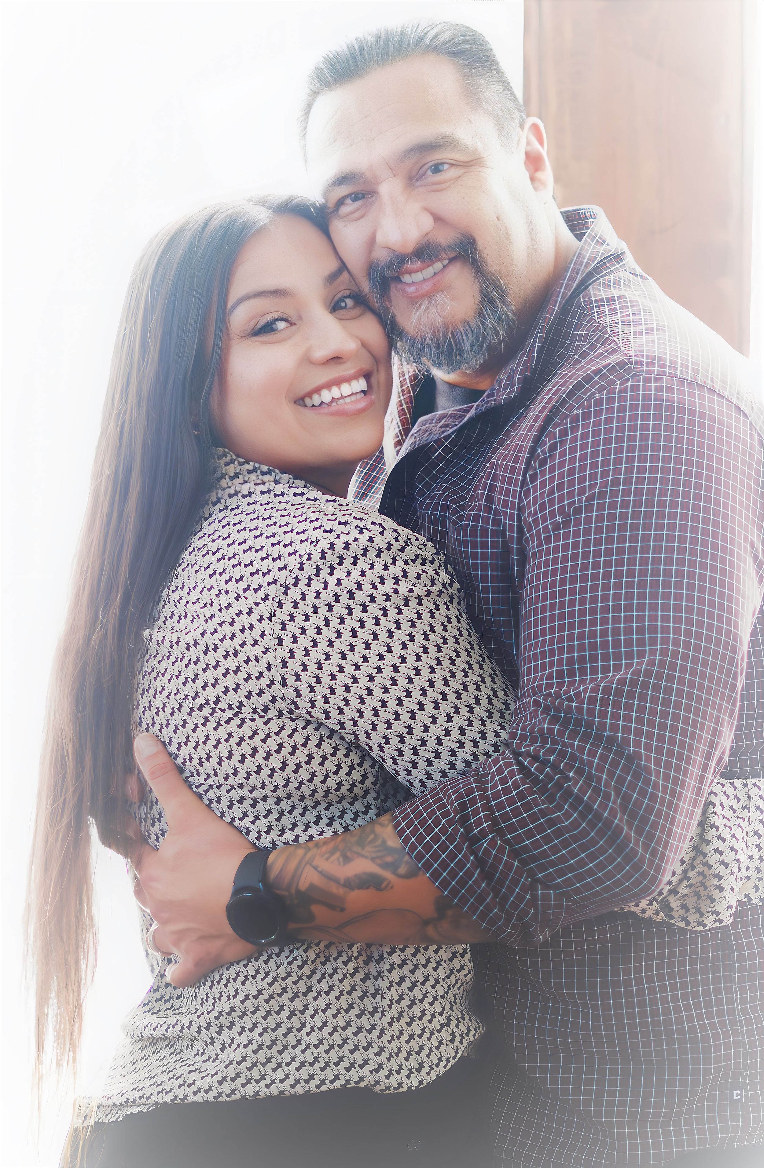Couple in warm sunlight sharing intimate embrace while smiling at camera.