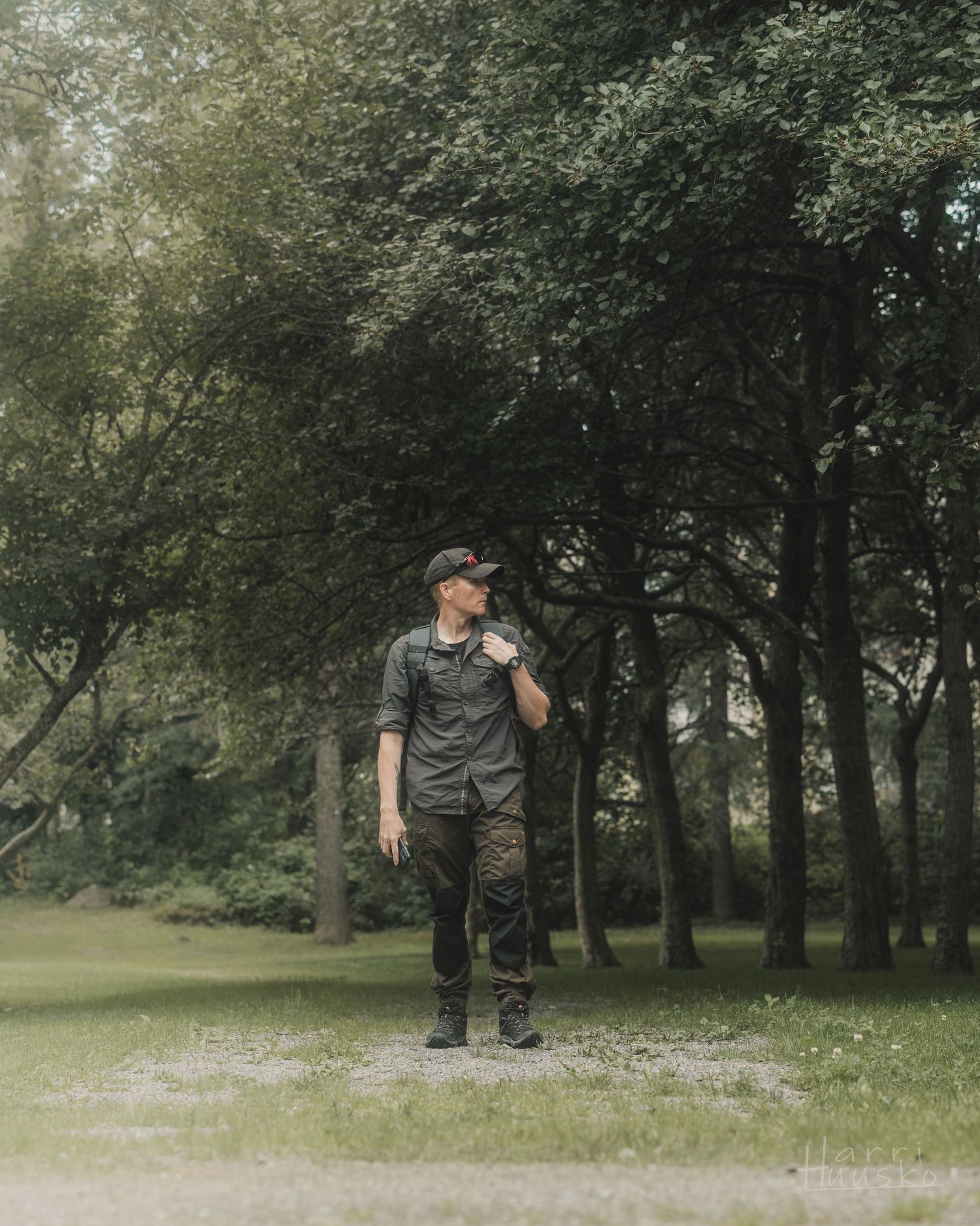 Person in casual attire standing on gravel path in misty green park.