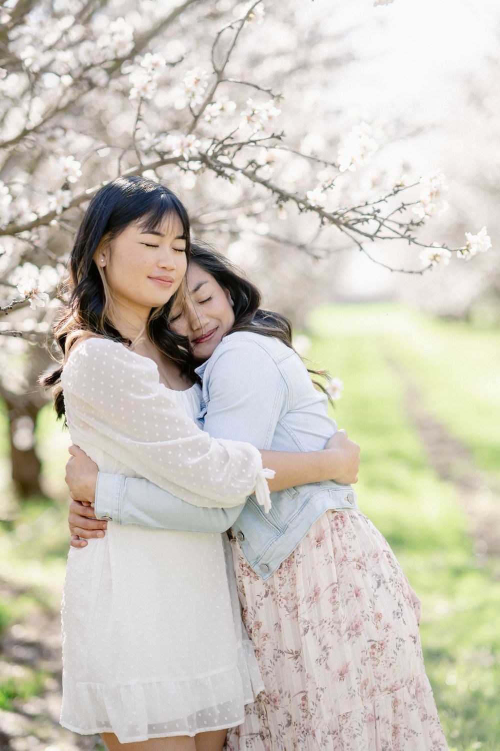 Two people share a tender embrace under blooming cherry blossom trees in a spring orchard.