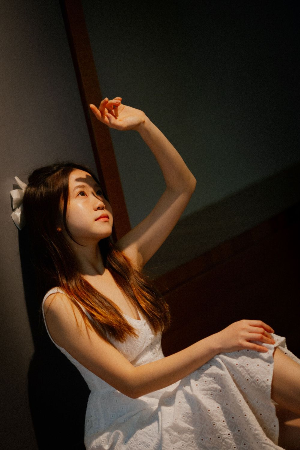 Person in white dress poses dramatically with raised arms in moody lighting.