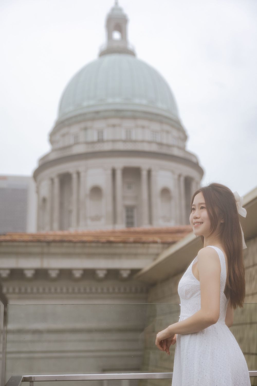 Person in white dress poses against architectural backdrop with domed building.