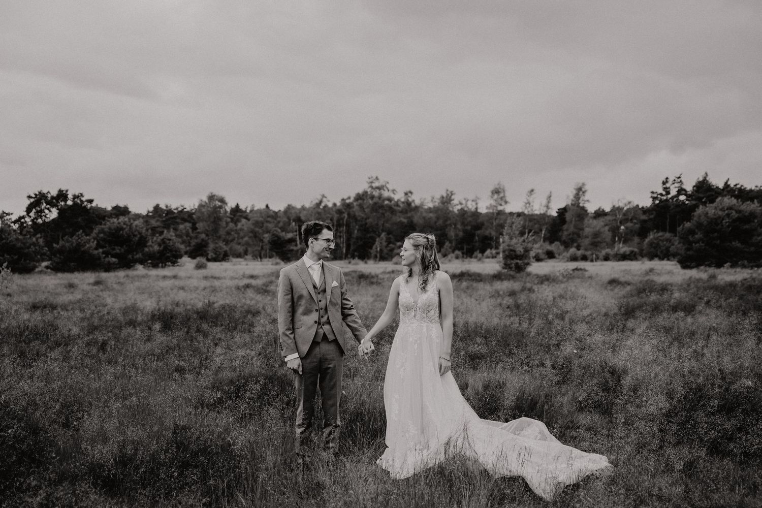 Black and white portrait of a wedding couple standing in an open field.
