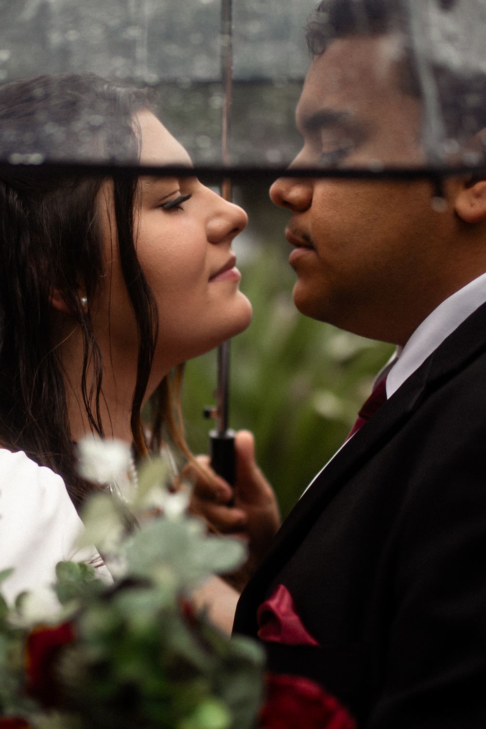 Close-up romantic moment under umbrella with roses and formal attire.