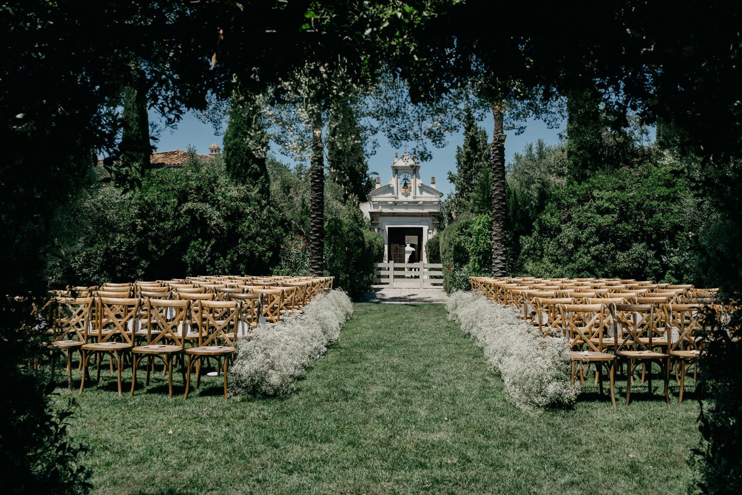 Outdoor wedding ceremony setup with wooden chairs and floral aisle decorations.