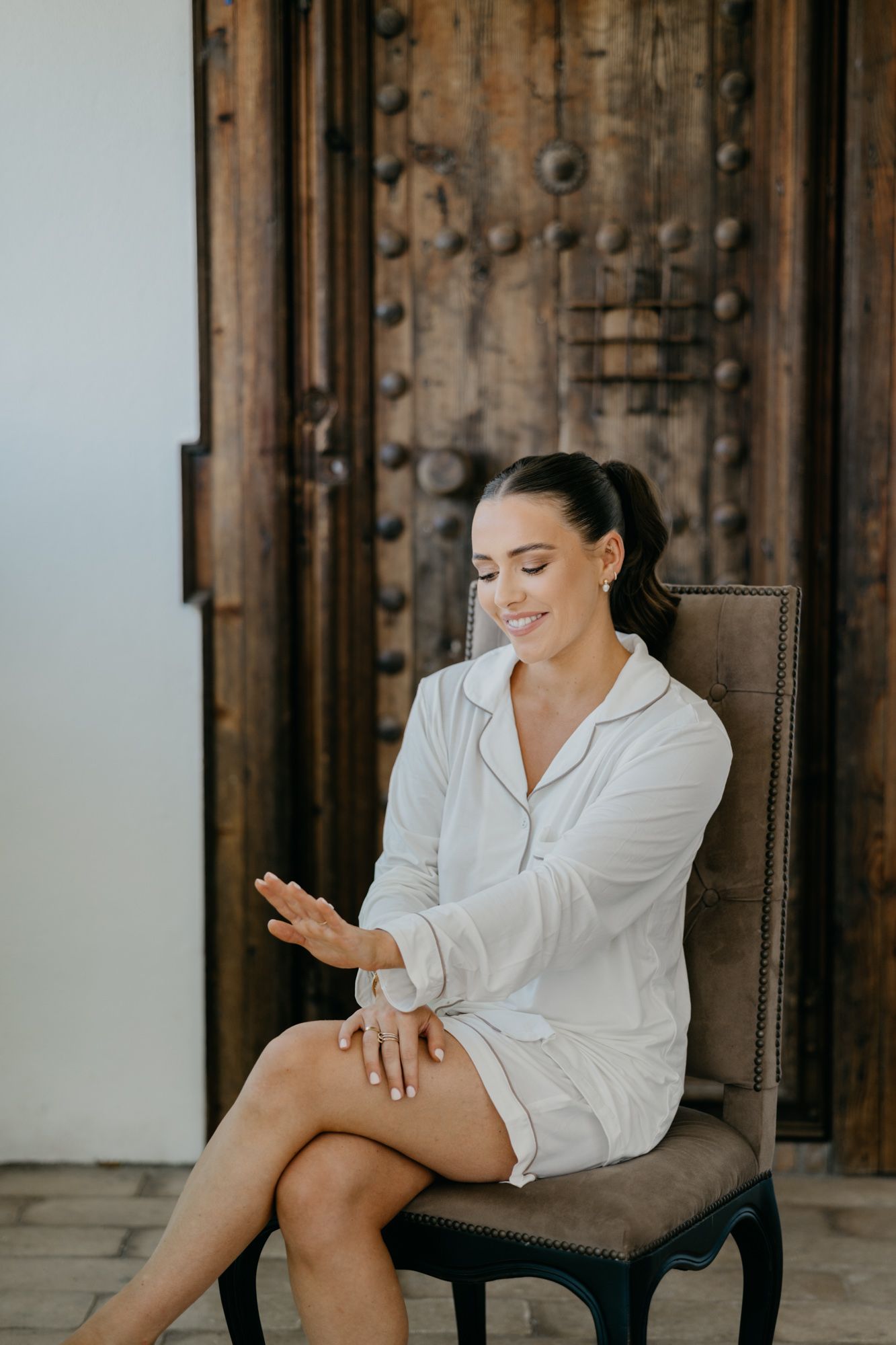 Woman in white loungewear relaxes in chair looking down at hands.