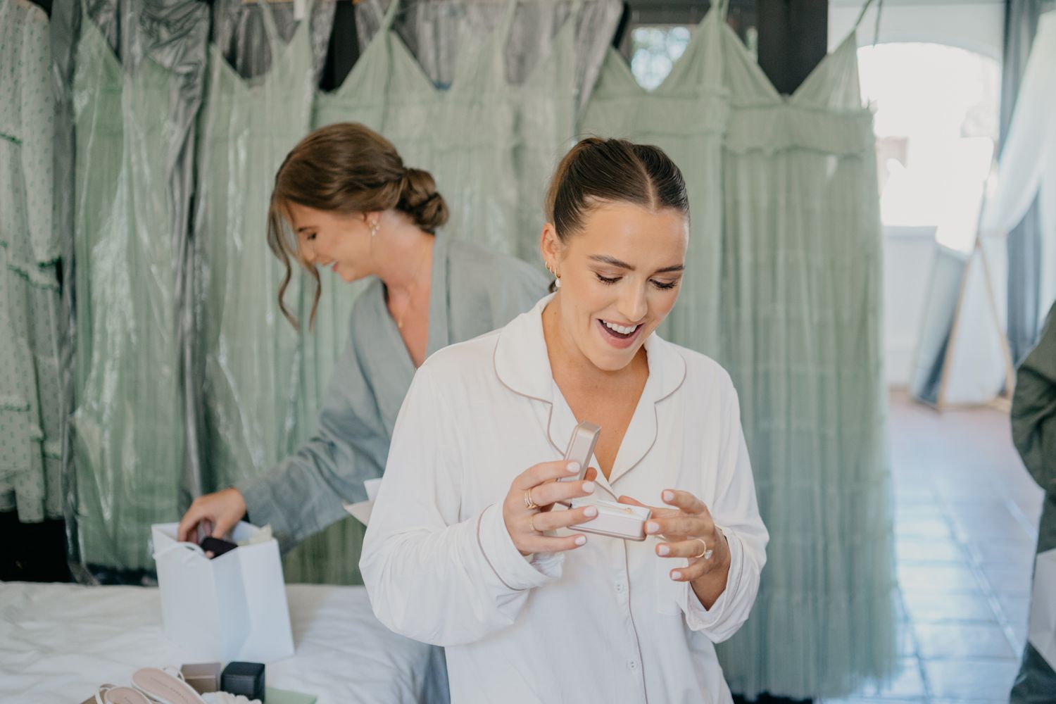 Women in robes prepare for event in room with hanging garments.