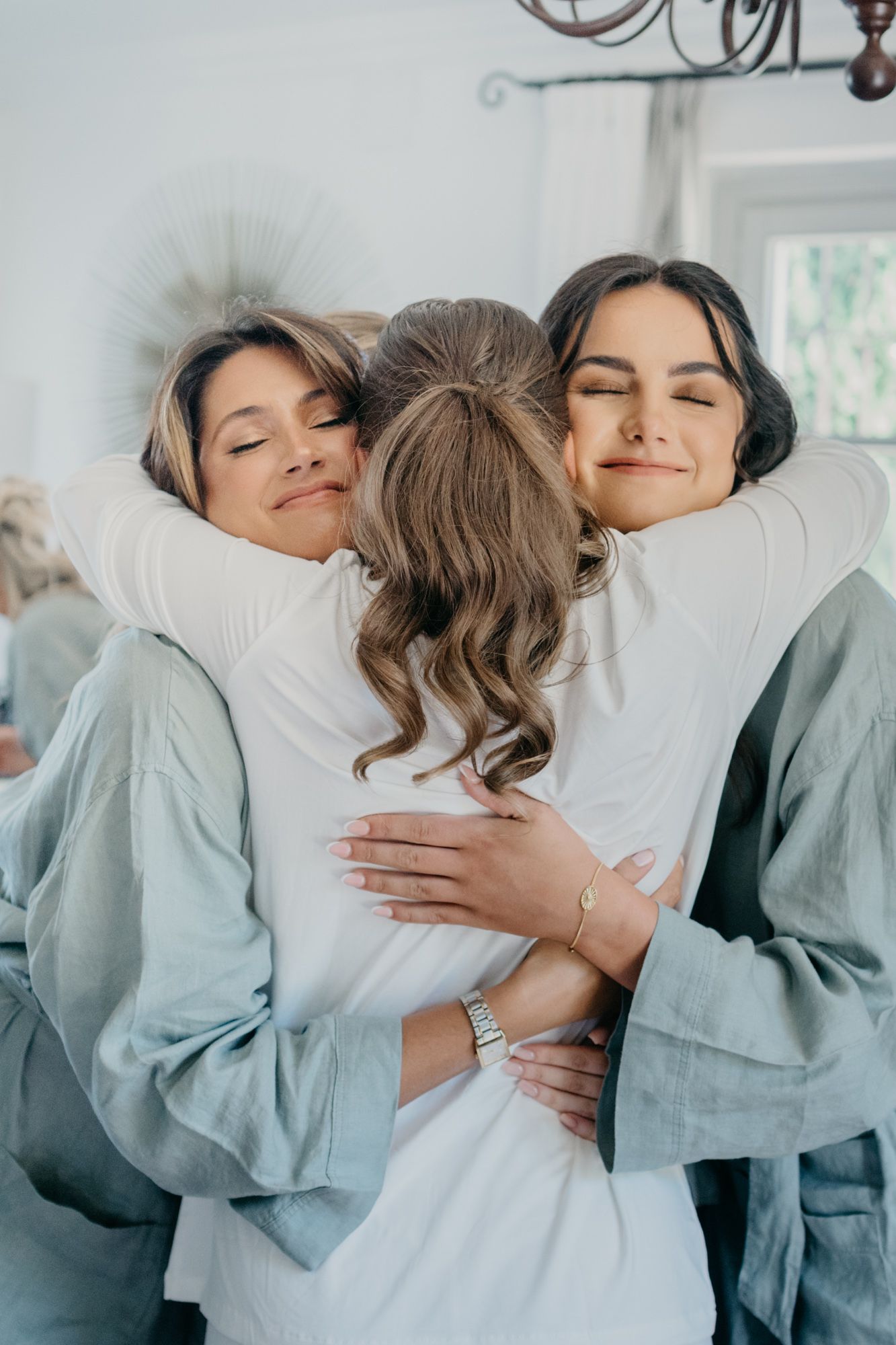 Three people share an emotional embrace while wearing matching robes during wedding preparations.