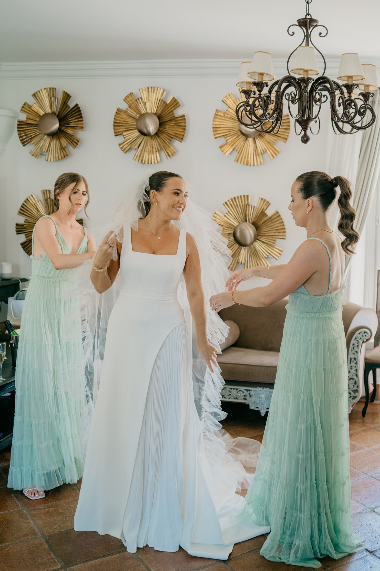 Bridesmaids in mint green gowns gather around bride in front of decorative gold wall art.