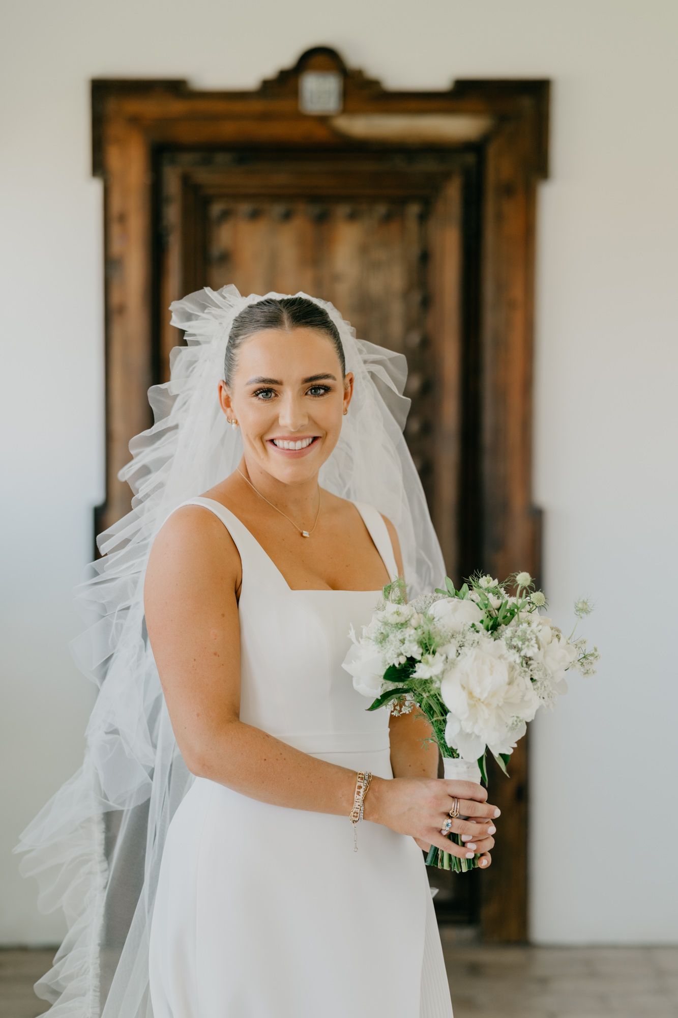 Bridal portrait in front of wooden door showing elegant white dress and flowing veil.