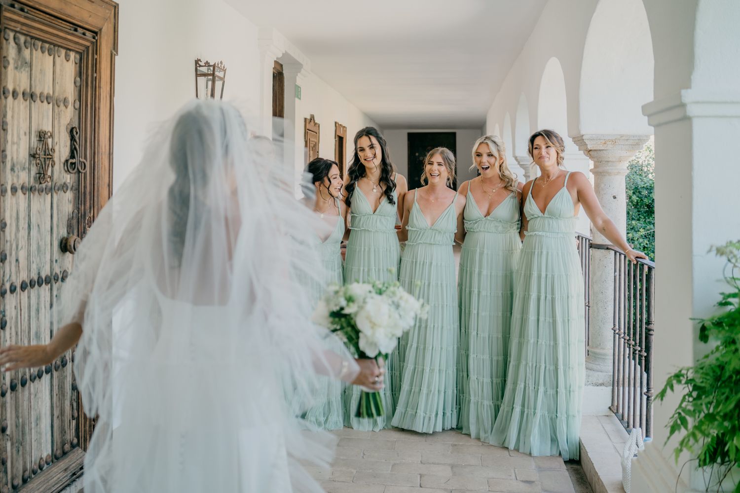 Wedding party in mint green bridesmaid dresses pose with bride in white on an elegant columned porch.