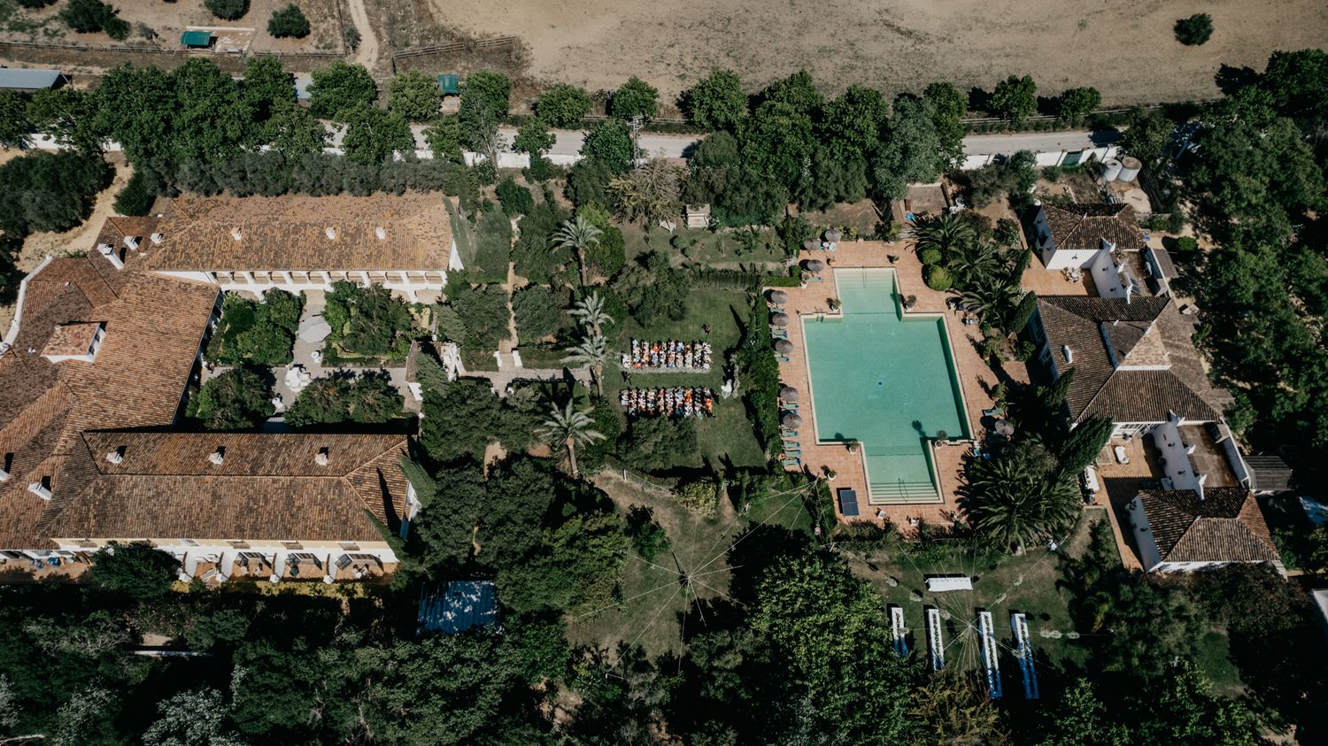 Bird's eye view of a luxury estate with swimming pool, gardens, and event spaces.