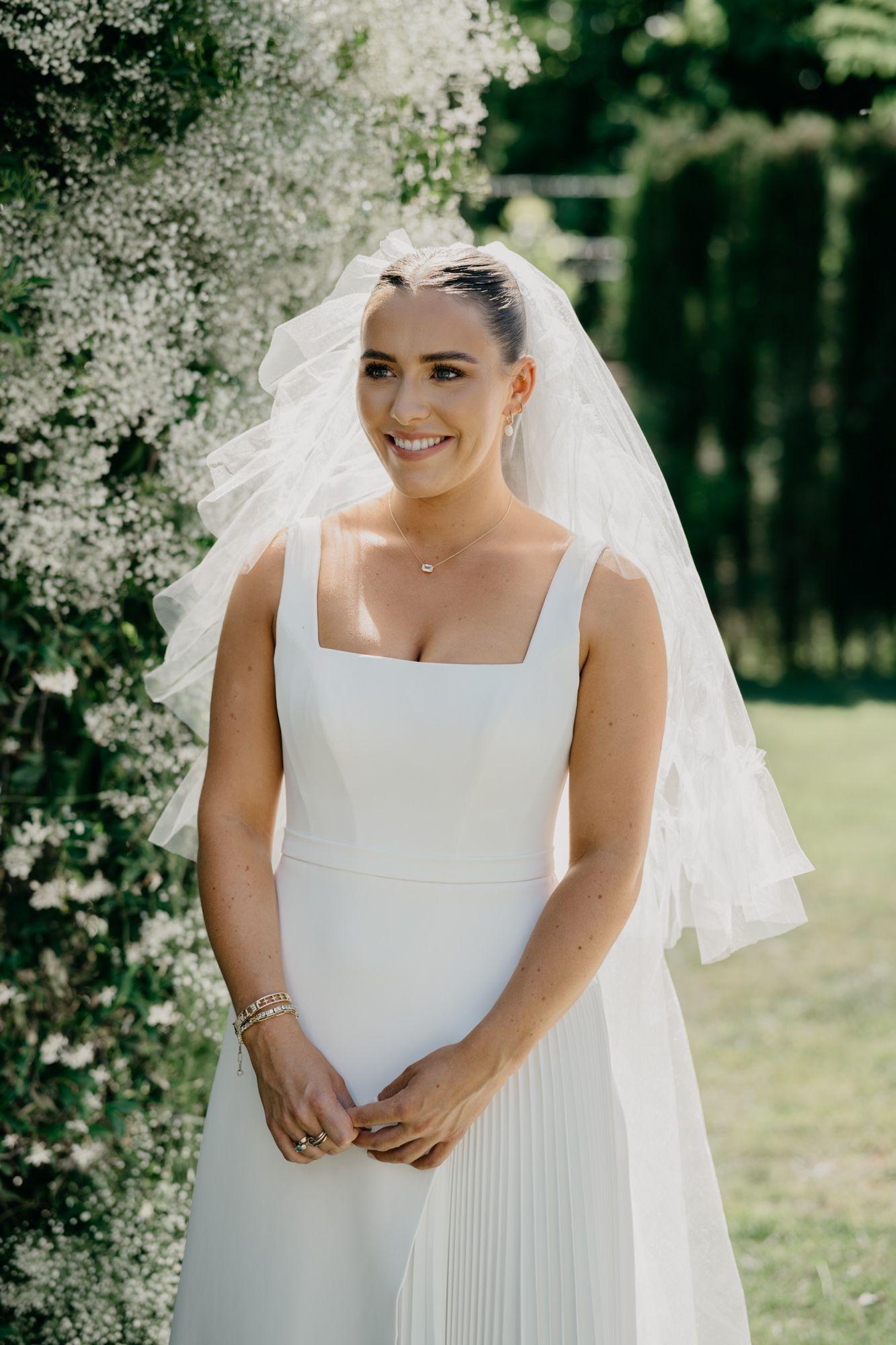 Classic white wedding dress with square neckline and flowing veil against garden greenery.
