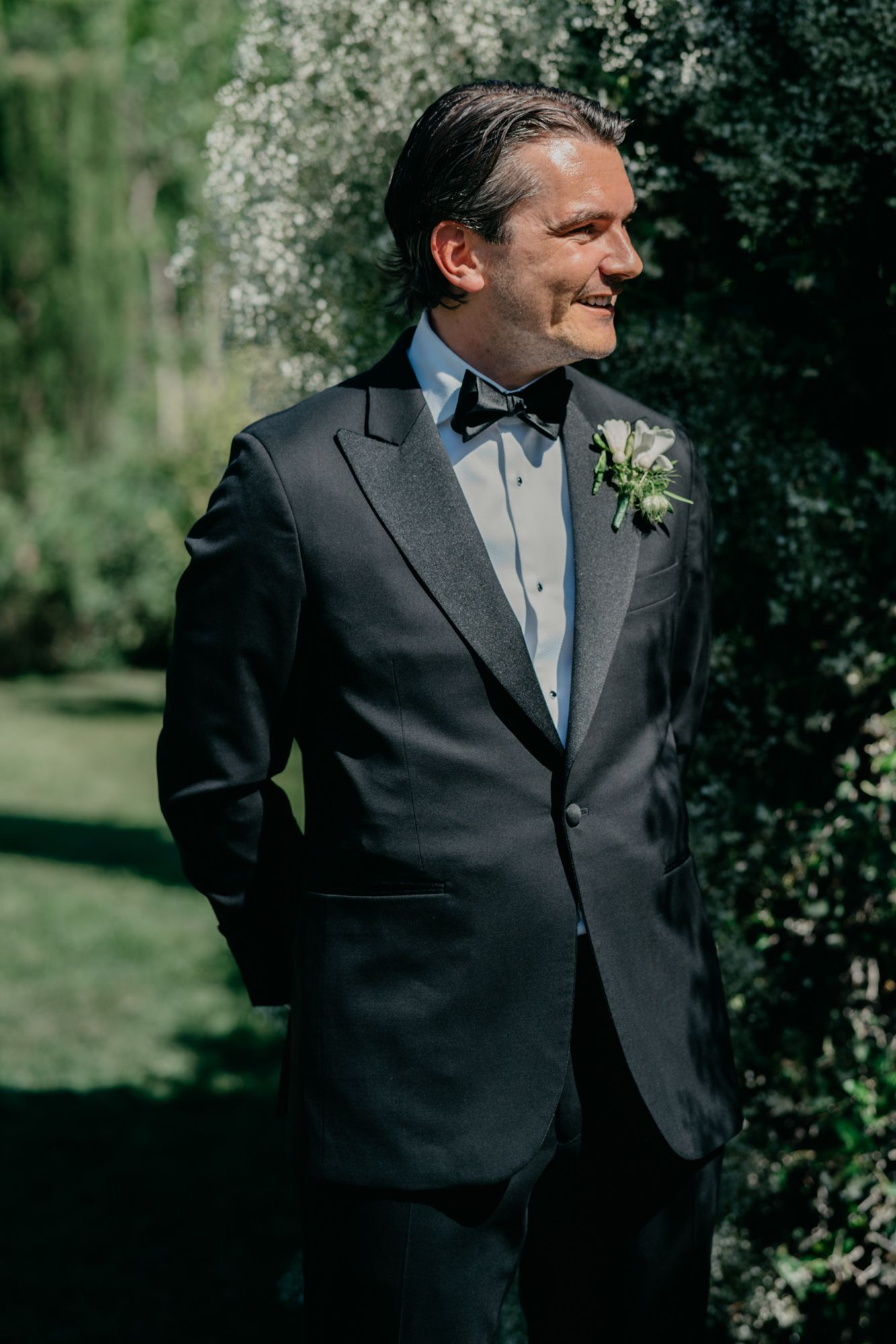 Classic black tuxedo with bow tie and boutonniere photographed in garden setting.