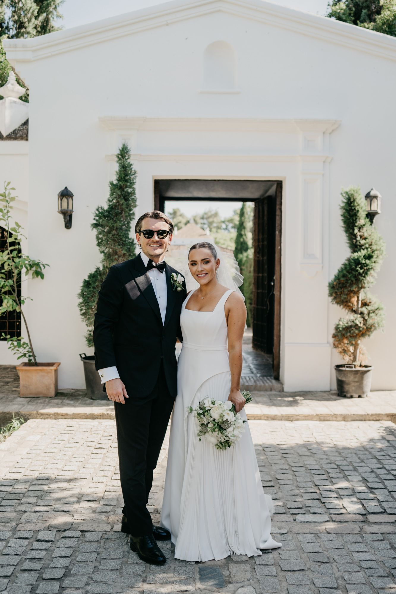 Classic wedding portrait in front of white stucco entrance with climbing vines.