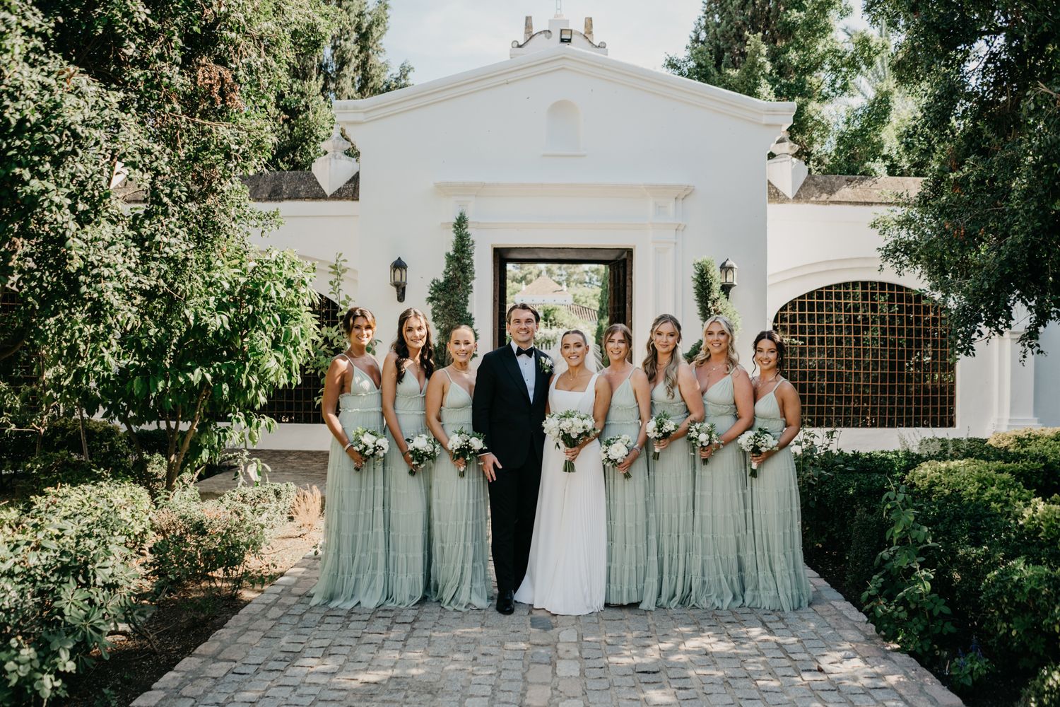 Wedding party with bridesmaids in sage green dresses at chapel entrance.
