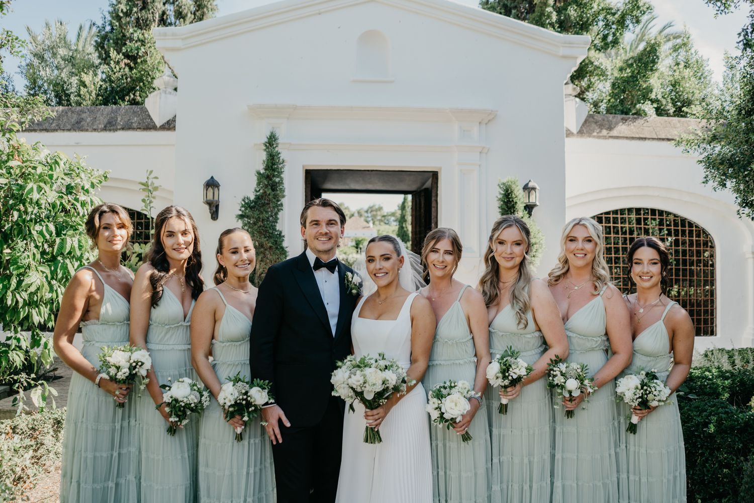 Wedding party stands together on stone patio with bridesmaids in light mint gowns.
