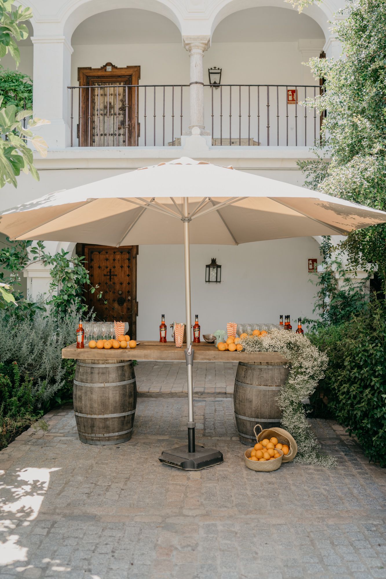 Outdoor bar setup with wooden barrels and white umbrella against Spanish colonial architecture.