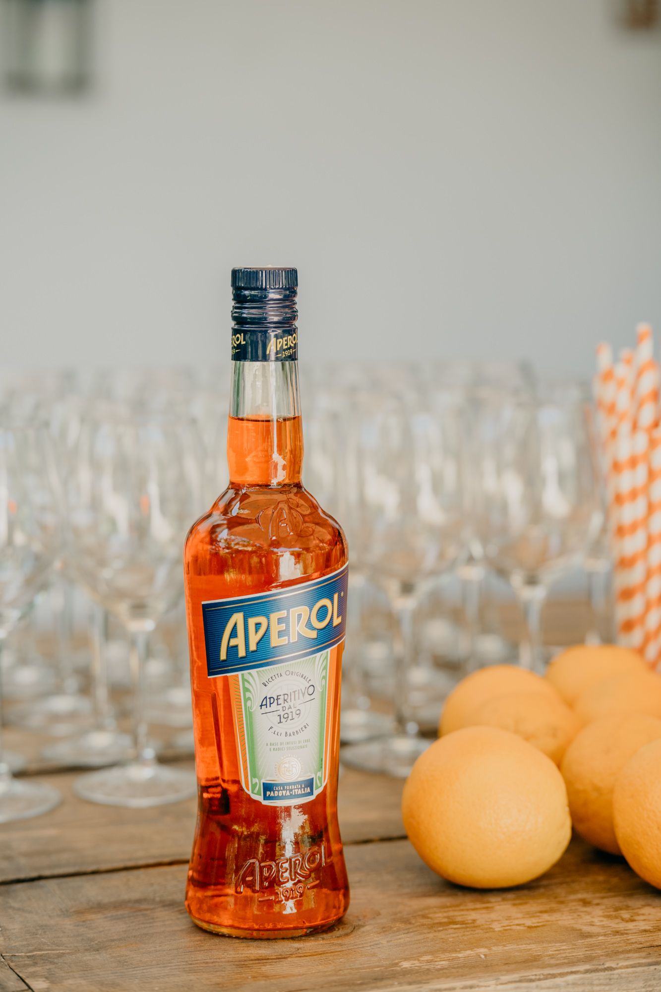 Bottle of Aperol with oranges and glassware on wooden bar setup.