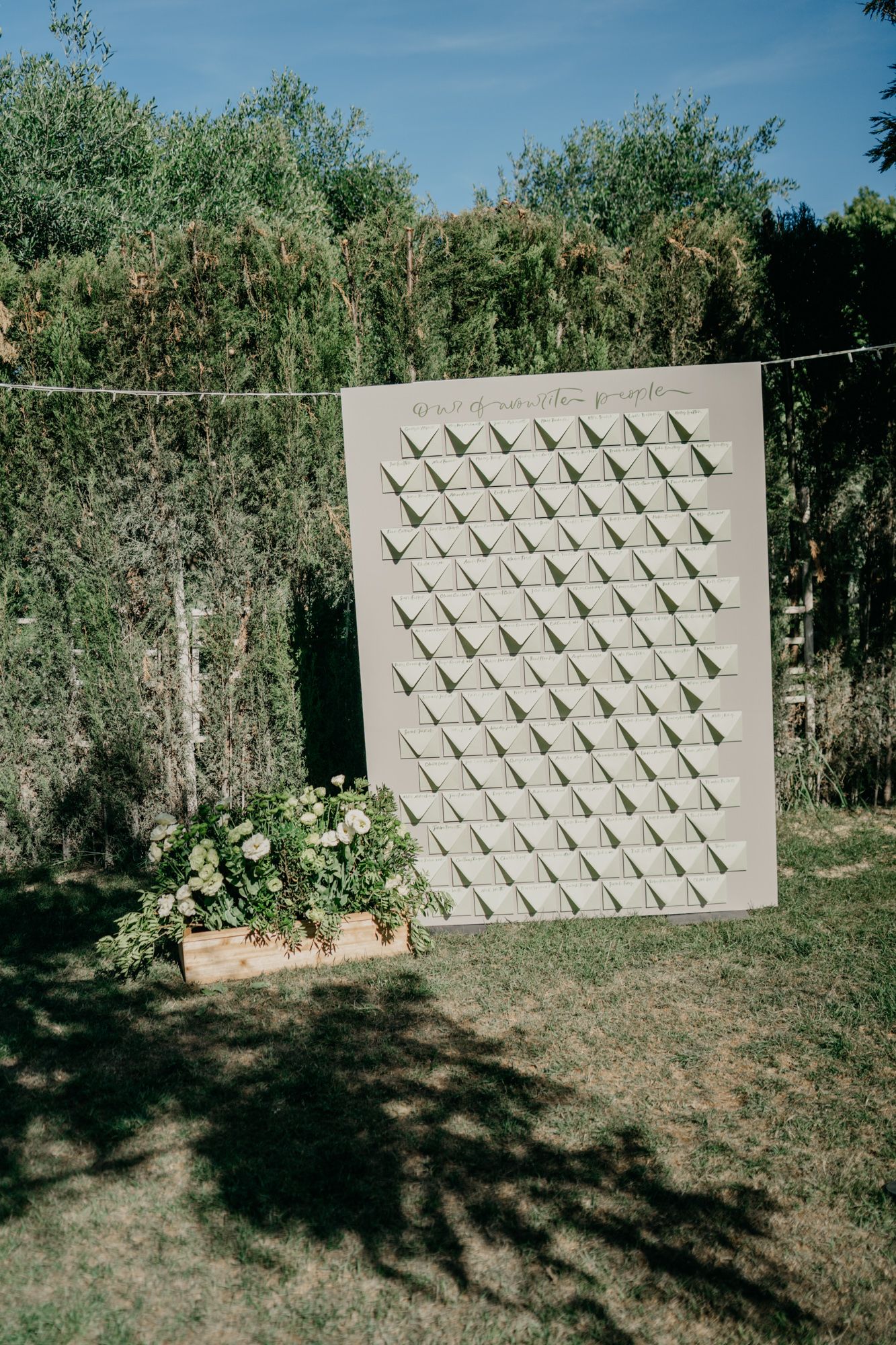 Modern geometric pattern display board hanging outdoors against green foliage.