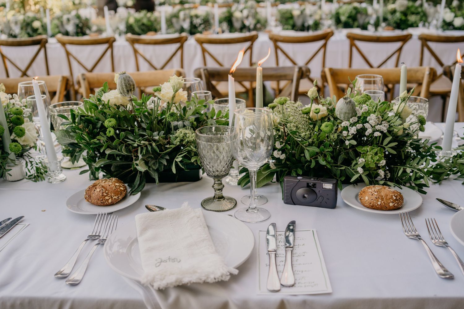 Close-up of wedding table place setting with rustic bread and lush green floral arrangements.